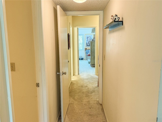 hallway featuring light colored carpet and a textured ceiling