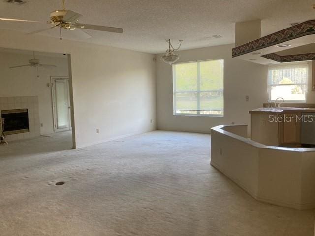 unfurnished living room with a textured ceiling, light colored carpet, ceiling fan, and a fireplace