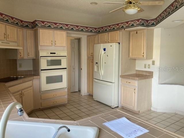 kitchen featuring white appliances, ceiling fan, light tile floors, custom range hood, and tile countertops