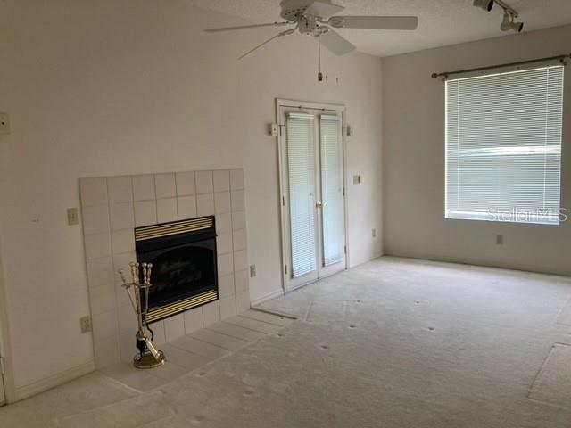 unfurnished living room with light carpet, ceiling fan, a tiled fireplace, and track lighting