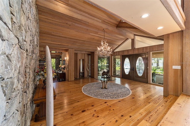 entrance foyer featuring a chandelier, wood walls, light hardwood / wood-style floors, high vaulted ceiling, and french doors