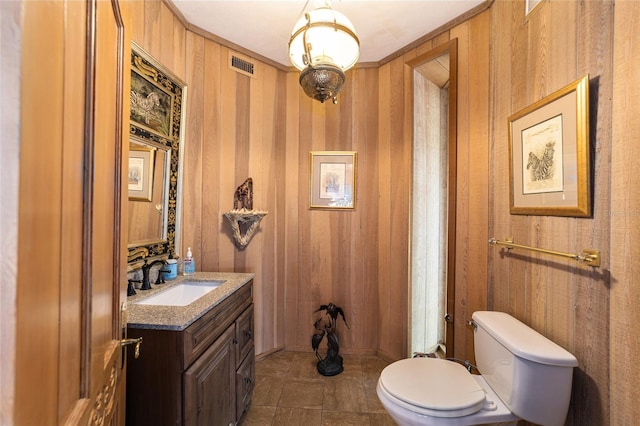 bathroom featuring wooden walls, vanity with extensive cabinet space, and toilet