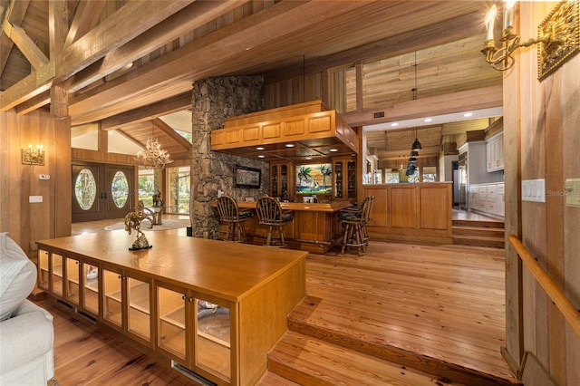 dining room featuring french doors, light hardwood / wood-style floors, wooden walls, and vaulted ceiling with beams