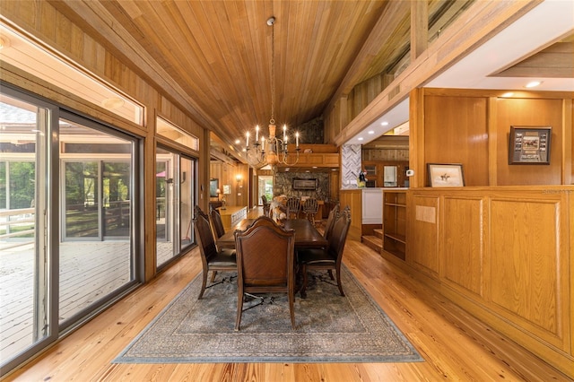 dining space featuring a notable chandelier, light hardwood / wood-style flooring, wooden ceiling, wooden walls, and a stone fireplace