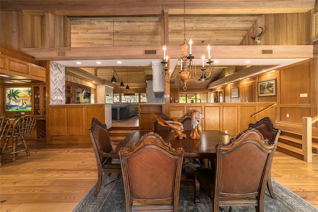 dining space with beam ceiling, wooden walls, a chandelier, and light wood-type flooring