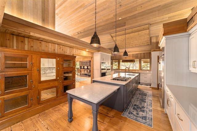 kitchen with pendant lighting, wood ceiling, white cabinets, light hardwood / wood-style floors, and a center island with sink