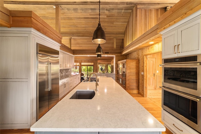 kitchen with sink, hanging light fixtures, appliances with stainless steel finishes, light hardwood / wood-style floors, and a center island with sink