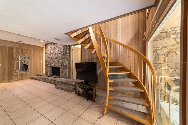 stairs with light tile flooring, wood walls, a stone fireplace, and a textured ceiling