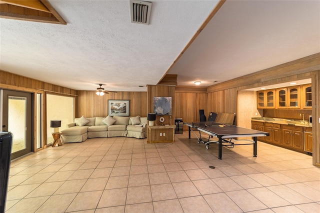 playroom featuring light tile floors, ceiling fan, a textured ceiling, wooden walls, and sink