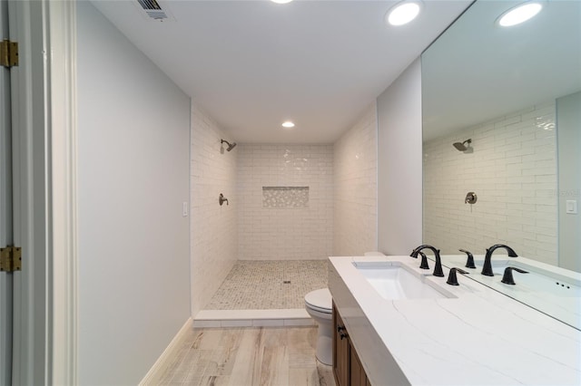 bathroom with wood-type flooring, toilet, vanity, and tiled shower