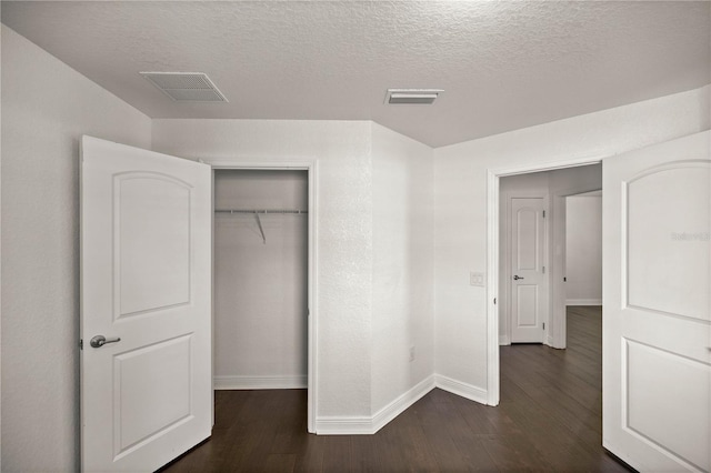 unfurnished bedroom with a textured ceiling, dark hardwood / wood-style flooring, and a closet