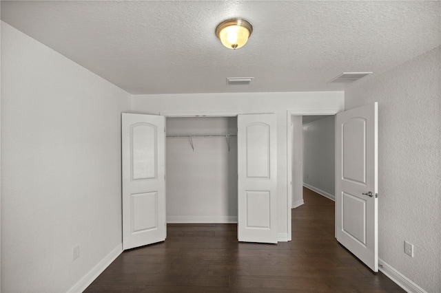 unfurnished bedroom featuring a textured ceiling, dark hardwood / wood-style flooring, and a closet