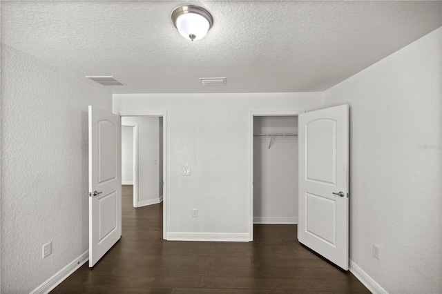 unfurnished bedroom with a textured ceiling, dark hardwood / wood-style flooring, and a closet