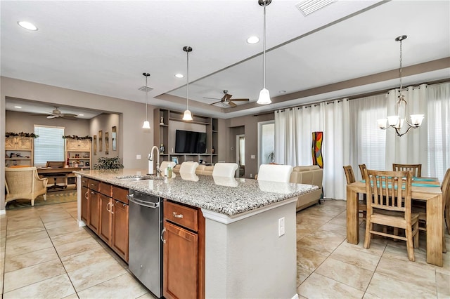 kitchen with an island with sink, light stone counters, decorative light fixtures, and ceiling fan with notable chandelier