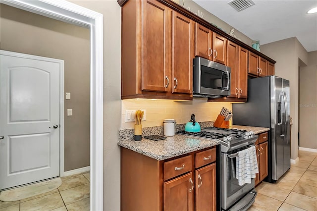 kitchen with backsplash, light tile flooring, appliances with stainless steel finishes, and light stone counters