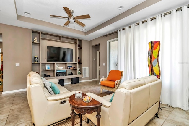 living room featuring light tile floors, a tray ceiling, and ceiling fan