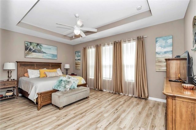 bedroom with ceiling fan, light hardwood / wood-style floors, and a raised ceiling