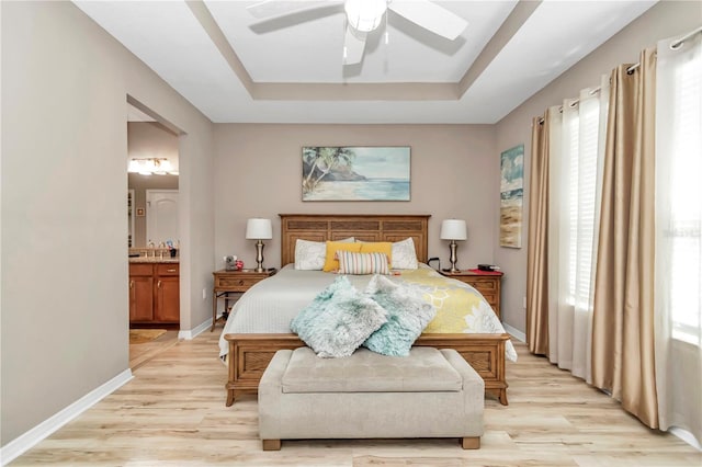 bedroom with a raised ceiling, ensuite bath, ceiling fan, and light wood-type flooring