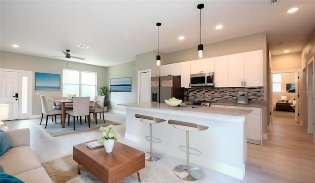 kitchen with ceiling fan, white cabinets, light hardwood / wood-style floors, stainless steel appliances, and decorative light fixtures