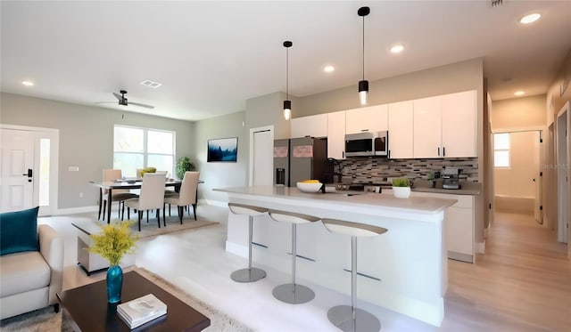 kitchen with an island with sink, pendant lighting, appliances with stainless steel finishes, tasteful backsplash, and white cabinetry