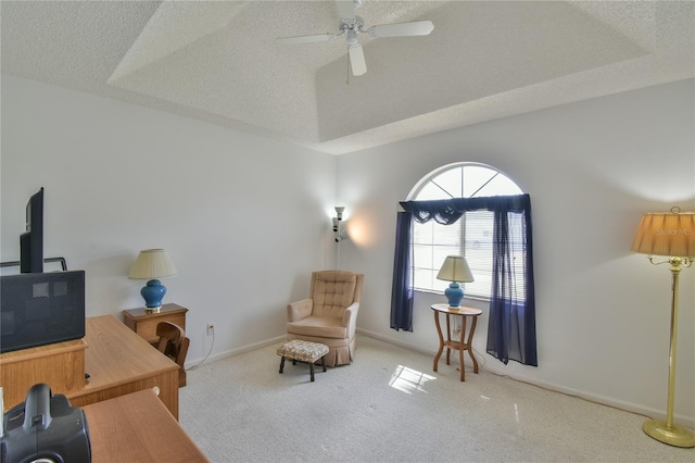 living area with ceiling fan, a textured ceiling, a raised ceiling, and light colored carpet