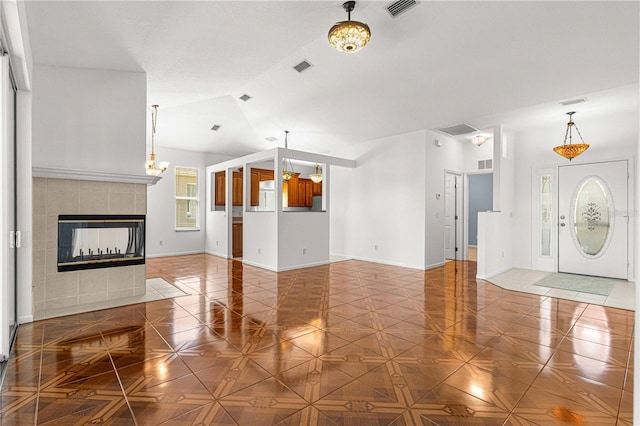 unfurnished living room featuring light tile flooring, lofted ceiling, a fireplace, and a chandelier