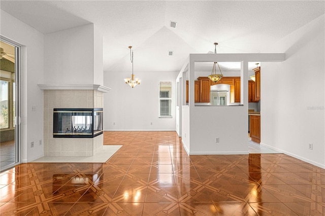 unfurnished living room featuring a chandelier, a tiled fireplace, light tile floors, and vaulted ceiling