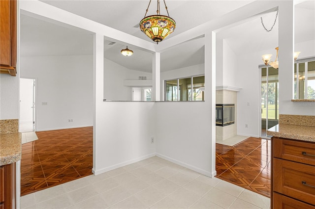 interior space featuring a tiled fireplace, pendant lighting, vaulted ceiling, and light tile floors