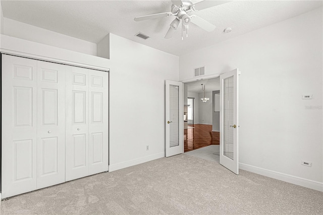 unfurnished bedroom with french doors, ceiling fan with notable chandelier, light carpet, and a closet