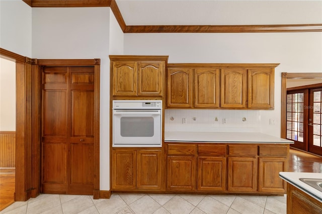 kitchen with french doors, light tile patterned flooring, crown molding, and oven