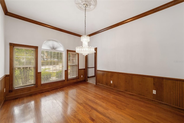 unfurnished room featuring a notable chandelier, wood-type flooring, wooden walls, and crown molding