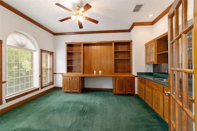 unfurnished office with built in desk, dark colored carpet, sink, ornamental molding, and ceiling fan