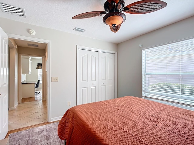 bedroom featuring ceiling fan, light tile patterned floors, a textured ceiling, and a closet