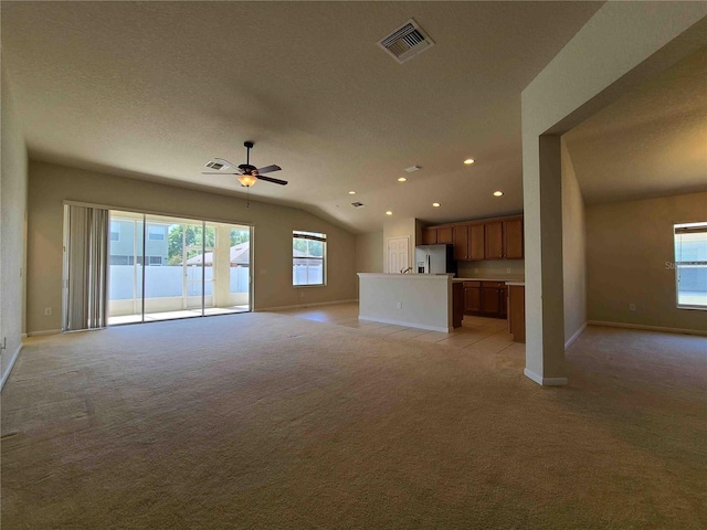 unfurnished living room with lofted ceiling, light carpet, ceiling fan, and a wealth of natural light