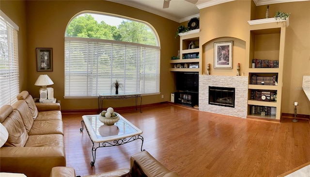 living room with built in features, ceiling fan, a fireplace, crown molding, and dark hardwood / wood-style floors