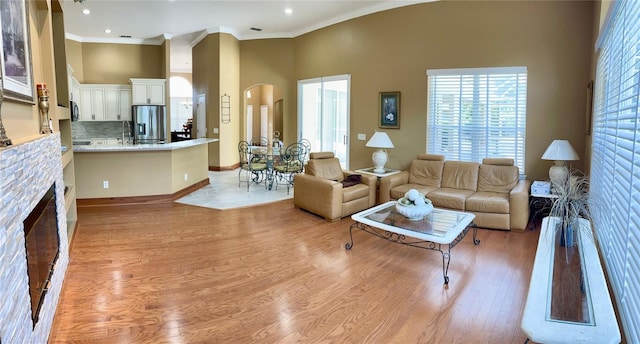 living room with crown molding, light hardwood / wood-style floors, a brick fireplace, and a towering ceiling