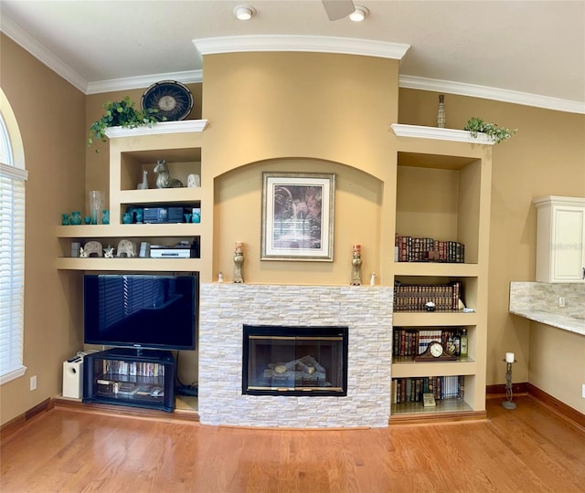 living room featuring a stone fireplace, crown molding, built in features, and wood-type flooring