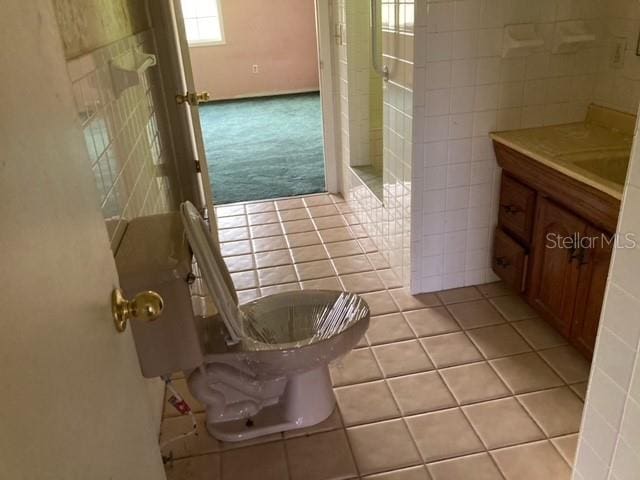 bathroom featuring vanity, toilet, tile floors, and tile walls