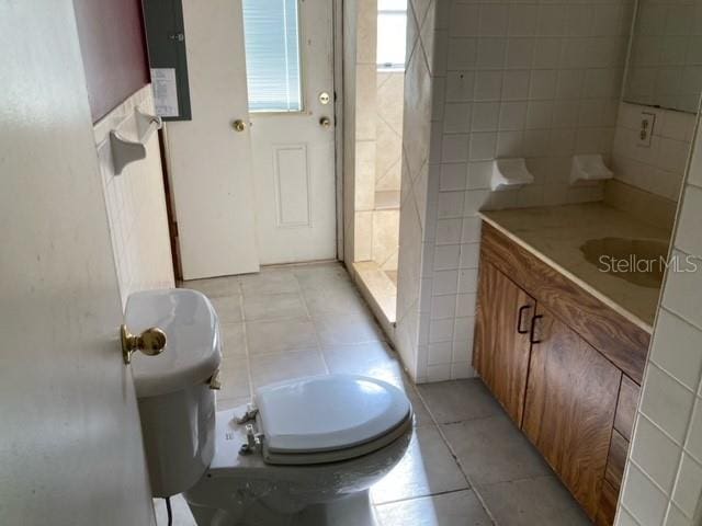 bathroom featuring tile floors, vanity, toilet, and tile walls