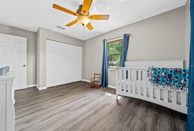 bedroom with wood-type flooring, ceiling fan, a nursery area, and a closet