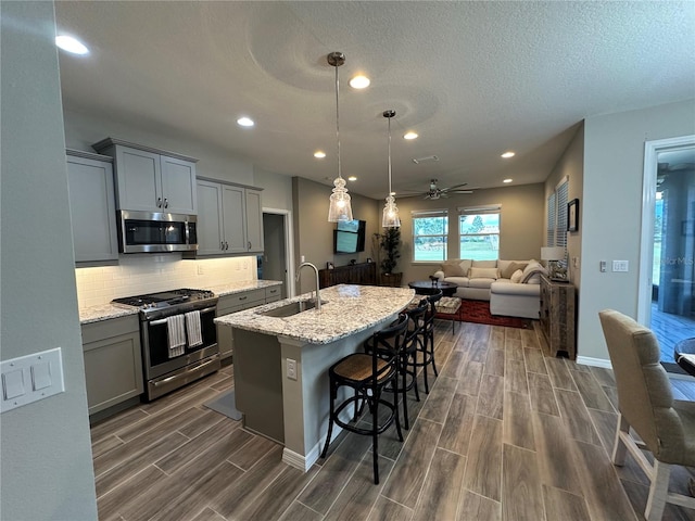 kitchen with appliances with stainless steel finishes, light stone countertops, a kitchen bar, dark hardwood / wood-style floors, and gray cabinetry