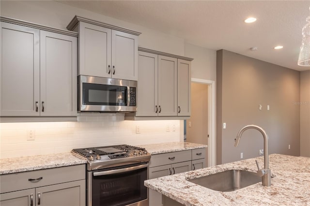 kitchen featuring sink, gray cabinets, appliances with stainless steel finishes, light stone counters, and tasteful backsplash