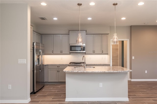 kitchen featuring light stone countertops, sink, hardwood / wood-style floors, stainless steel appliances, and decorative light fixtures