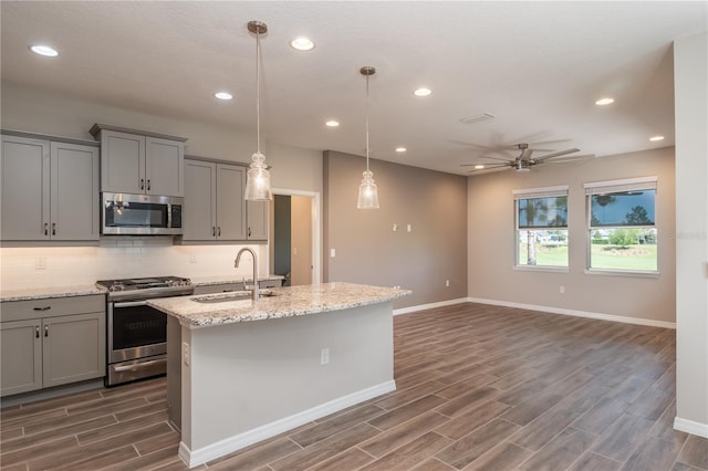 kitchen with ceiling fan, appliances with stainless steel finishes, a kitchen island with sink, dark hardwood / wood-style floors, and sink