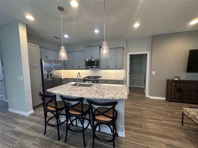 kitchen with dark hardwood / wood-style flooring, an island with sink, sink, pendant lighting, and stainless steel appliances