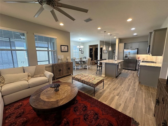 living room featuring sink, light hardwood / wood-style flooring, and ceiling fan with notable chandelier