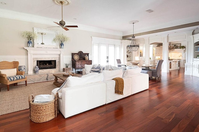 living room with ceiling fan with notable chandelier, dark hardwood / wood-style floors, crown molding, and a fireplace