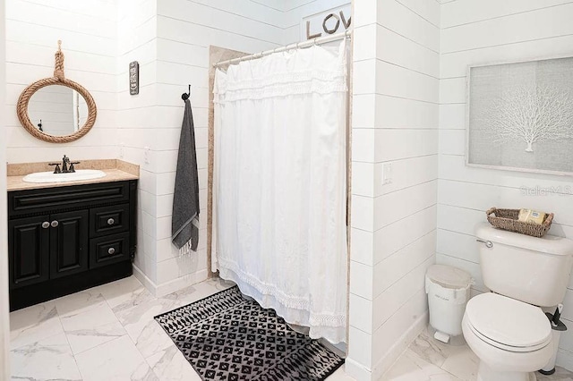 bathroom featuring toilet, vanity, and wood walls