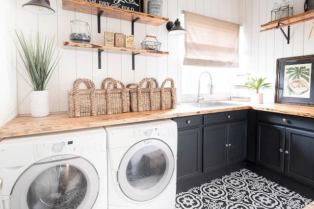 laundry area featuring dark tile patterned flooring, washing machine and dryer, sink, wooden walls, and cabinets