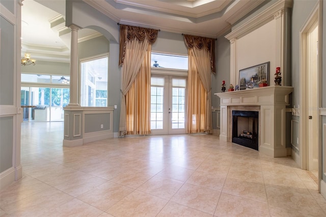 unfurnished living room with a chandelier, a raised ceiling, ornamental molding, and french doors